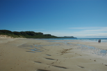 Picture of a wide beach with golden sand at a wide bay, two people on the beach close to the water