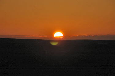 Picture of the sun disappearing behind some hills